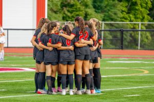 The Bernards Girls Soccer team huddles before their home opener. Photo used with permission from dunnder_media