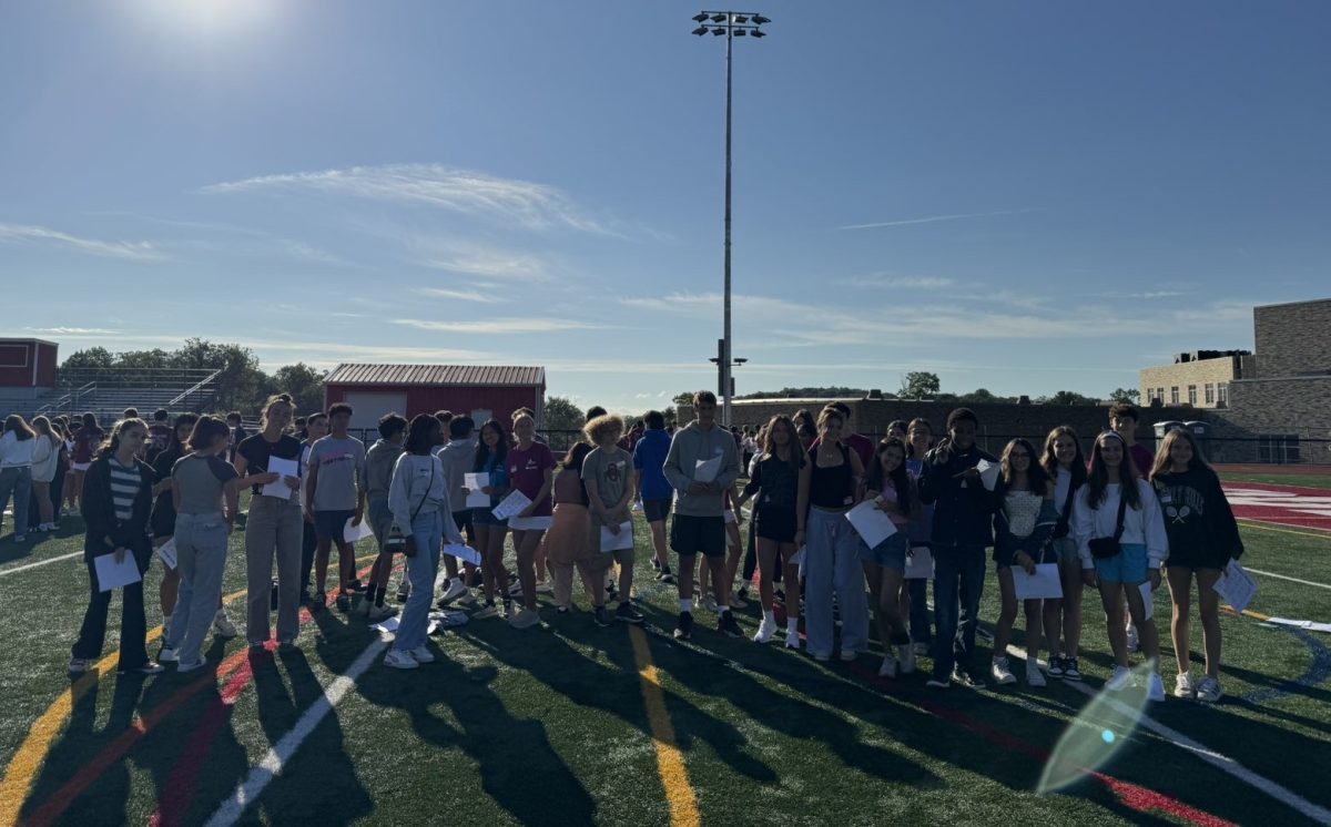 Freshman poses on the turf with the Peer Leaders at orientation