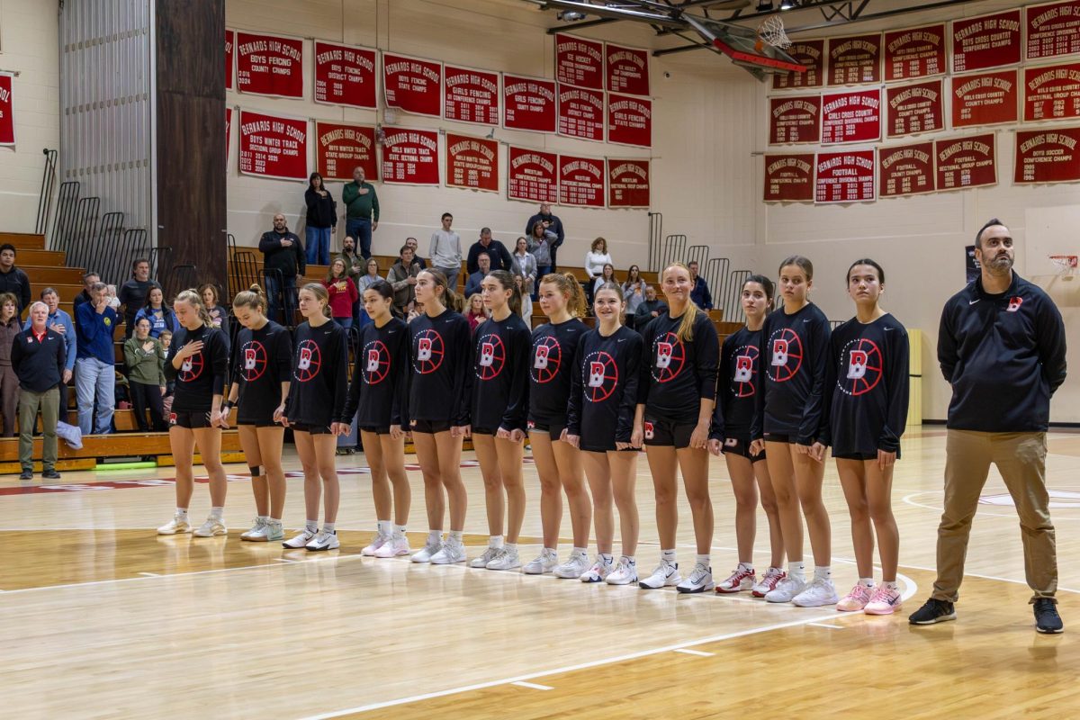 The girls basketball team stands on the court for the National Anthem before a win against Voorhees